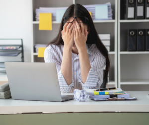 Picture of a lady behind a laptop with her head in her hands